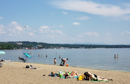 A sandy beach scene with people sunbathing, swimming, and enjoying the water under a clear blue sky.