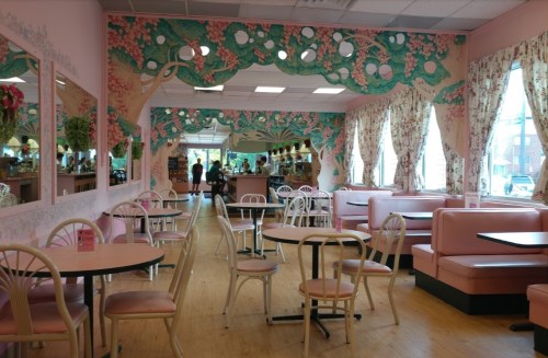A pastel-colored café interior with pink booths, floral wallpaper, and large mirrors reflecting a cozy atmosphere.