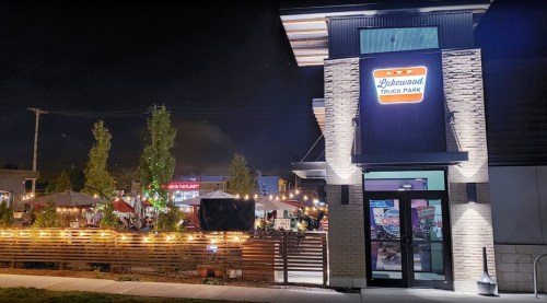 A vibrant food truck park at night, featuring outdoor seating and illuminated signage.