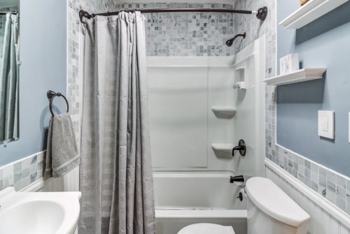 A small bathroom featuring a shower-tub combo, gray shower curtain, and light blue walls with decorative tiles.