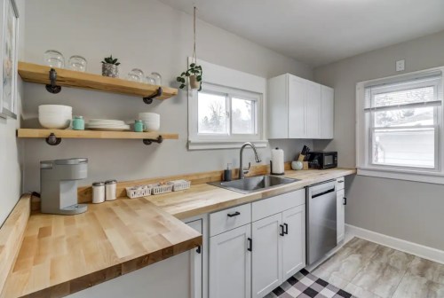 Modern kitchen with wooden countertops, open shelves, and white cabinets, featuring a sink and stainless steel appliances.