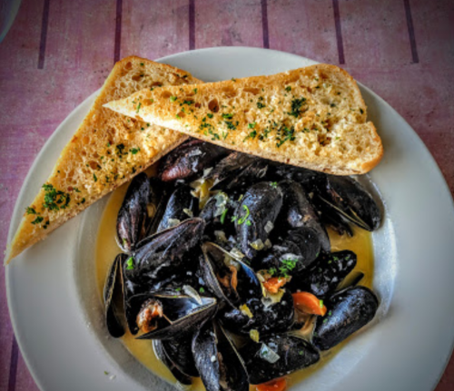 A plate of mussels in broth served with two slices of garlic bread on the side.