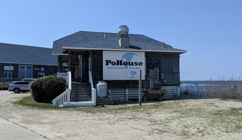 A waterfront dining restaurant named PoHouse, featuring a wooden exterior and a clear blue sky in the background.
