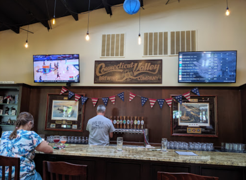 A bar with a wooden counter, two TVs showing sports, and a bartender serving drinks, decorated with patriotic banners.