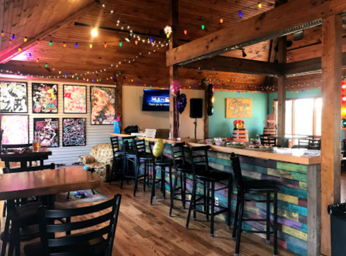 A vibrant bar area with colorful artwork, wooden beams, and festive lights, creating a lively atmosphere.