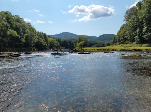 A serene river flows through a lush green landscape, with mountains in the background under a clear blue sky.