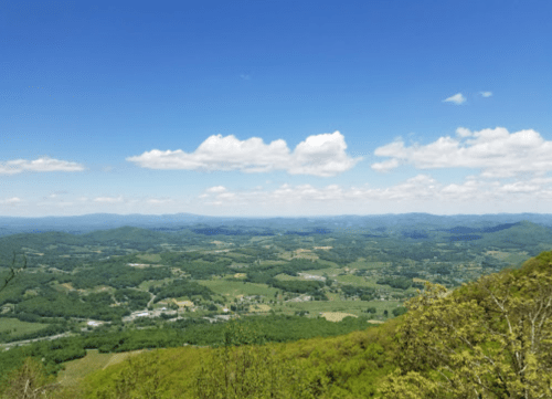 A panoramic view of lush green mountains and valleys under a bright blue sky with fluffy white clouds.