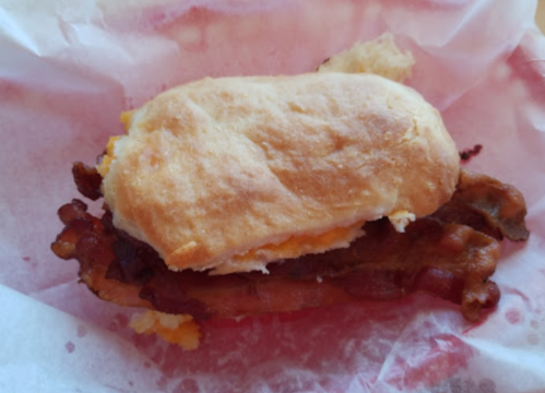 A sandwich with a soft bun, crispy bacon, and melted cheese, resting on red paper.