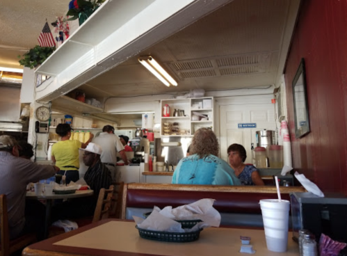 A cozy diner interior with patrons at tables, a visible kitchen area, and decor featuring American flags.