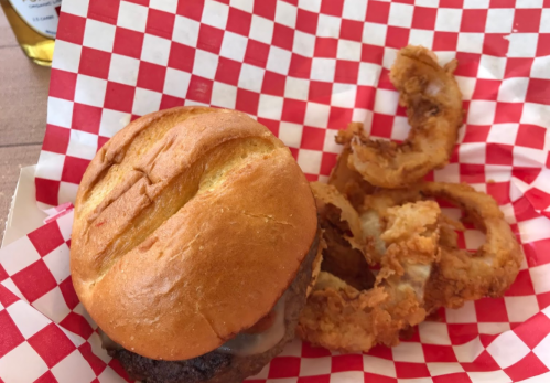 A burger on a red and white checkered paper, accompanied by crispy onion rings.