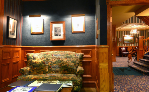 Cozy sitting area with a patterned couch, wooden paneling, and framed artwork on the walls. Warm, inviting atmosphere.