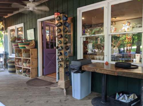A cozy porch with colorful baskets, a purple door, and a table beside a trash can, inviting a warm atmosphere.