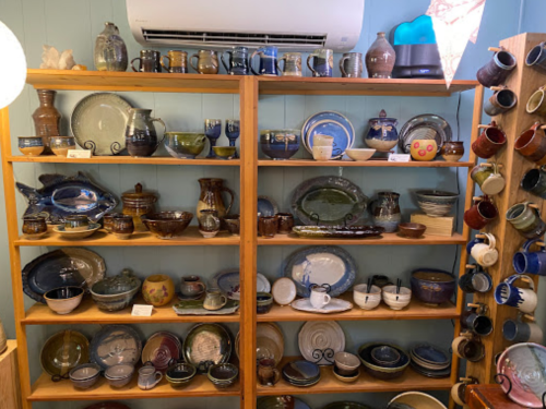A wooden shelf displaying a variety of colorful pottery, including bowls, mugs, and decorative pieces.