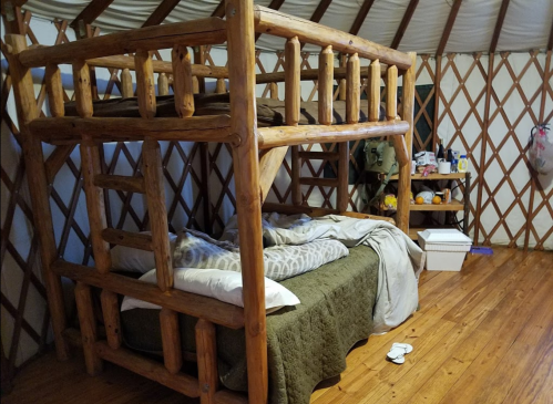 A cozy yurt interior featuring a wooden bunk bed and a lower bed with bedding, surrounded by wooden walls.