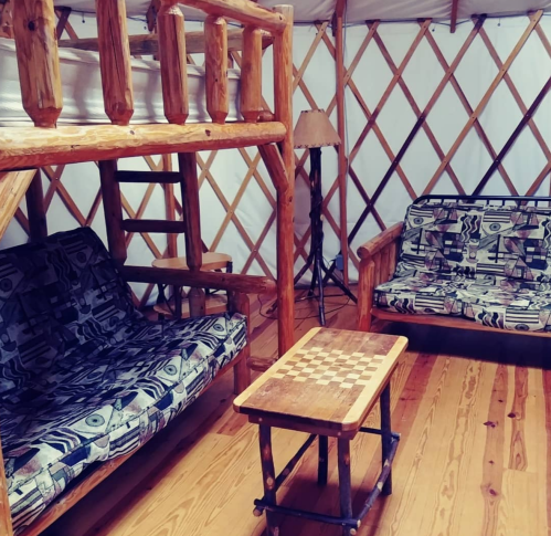 Cozy interior of a yurt featuring a lofted bed, seating area, and a wooden table with a checkerboard pattern.
