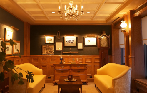 Cozy room with two yellow armchairs, a wooden table, framed pictures, and a vintage clock under a chandelier.