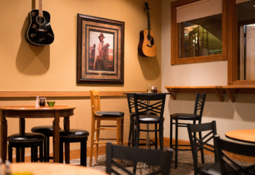 Cozy restaurant interior with wooden tables, black chairs, and guitars hanging on the wall. A framed picture is displayed.