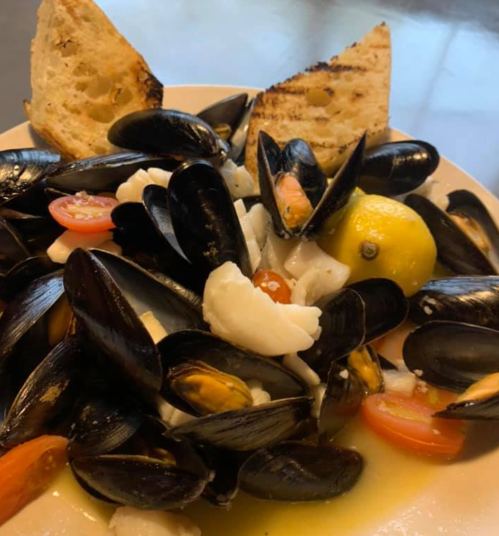 A plate of mussels with lemon, cherry tomatoes, and grilled bread slices.