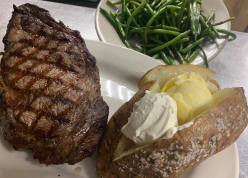 A grilled steak with grill marks, a baked potato topped with butter and sour cream, and a side of green beans.