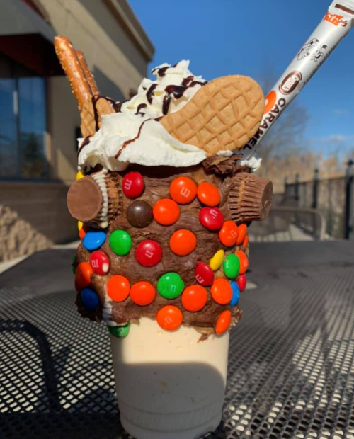 A decadent milkshake topped with whipped cream, chocolate drizzle, cookies, pretzels, and colorful candy.