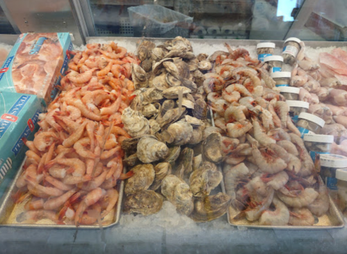 A seafood display featuring shrimp and oysters on ice, with containers of seafood products nearby.