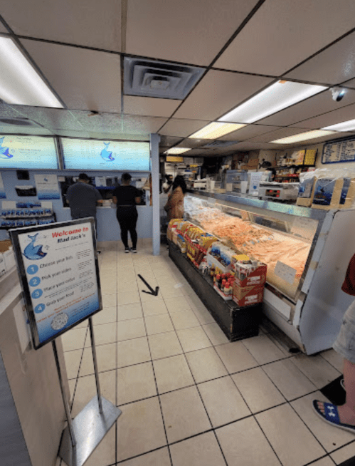 Interior of a seafood market with customers at the counter and a display of fresh fish and seafood. Signage visible.