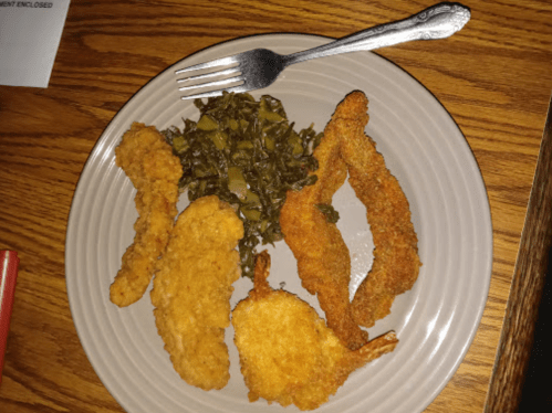 A plate with fried shrimp, chicken tenders, and collard greens, with a fork resting on the side.