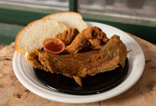 A plate of fried fish with a side of bread and a small cup of sauce.