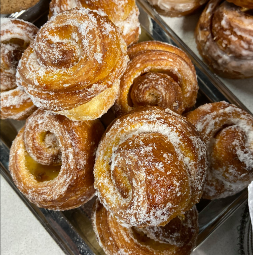 A close-up of golden, sugary pastries arranged on a tray, showcasing their spiral shapes and sweet coating.