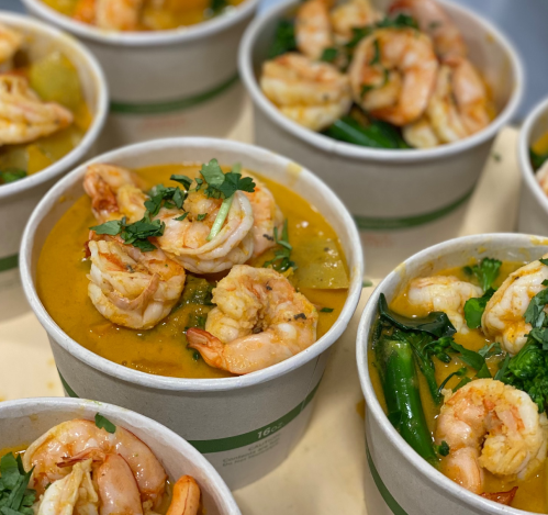 Bowls of shrimp curry with fresh herbs and vegetables, served in eco-friendly containers.