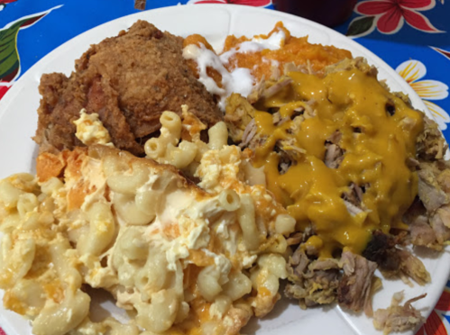 A plate of comfort food featuring fried chicken, macaroni and cheese, pulled pork with cheese, and sweet potato casserole.