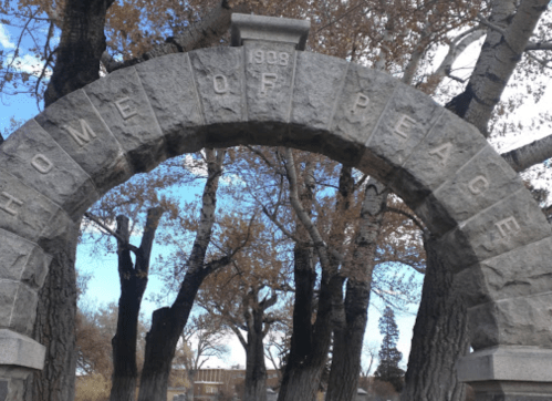 Stone archway inscribed with "Home of Peace," surrounded by trees and a clear blue sky.