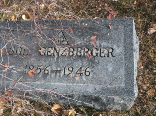 A weathered gravestone with the name "Sol Genzenberger" and the years "1856-1946," surrounded by dry leaves and grass.