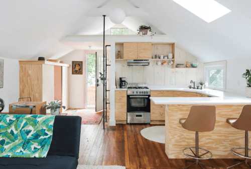 Bright, modern kitchen with wooden cabinets, a central island, and a cozy living area featuring a black sofa and colorful throw.