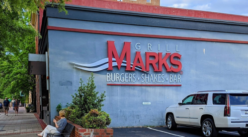 Sign for Grill Marks featuring "Burgers, Shakes, Bar" on a blue wall, with a person sitting nearby.