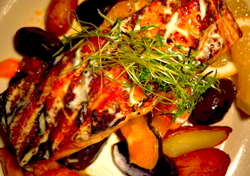 Grilled salmon fillet topped with herbs, served with colorful roasted vegetables and lemon slices.