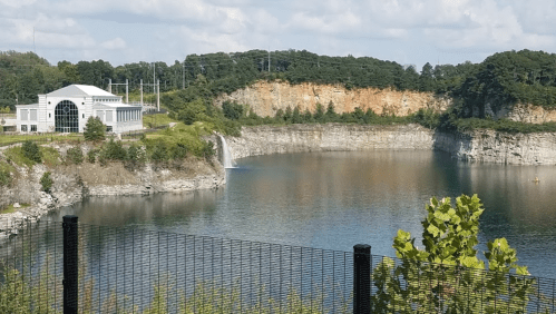 A scenic view of a lake surrounded by cliffs, with a modern building and greenery in the foreground.