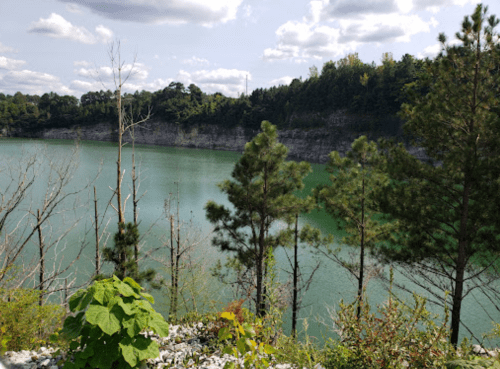 A serene lake surrounded by rocky cliffs and lush greenery under a partly cloudy sky.