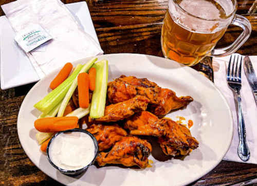 A plate of buffalo chicken wings with celery, carrots, and ranch dressing, alongside a glass of beer.