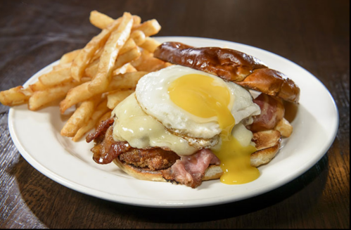 A sandwich with a fried egg, bacon, and cheese on a bun, served with crispy French fries on the side.