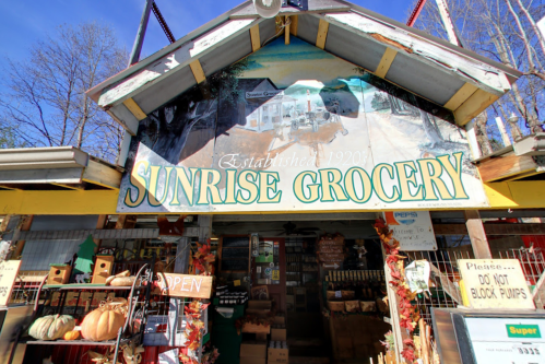 Front view of Sunrise Grocery, featuring a colorful sign and autumn decorations, with an open sign visible.