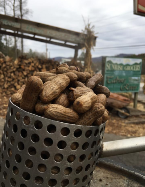 A metal cup filled with raw peanuts, with a rustic background of wood piles and a sign.