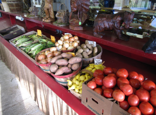 A display of fresh vegetables, including tomatoes, sweet potatoes, and onions, alongside wooden carvings.