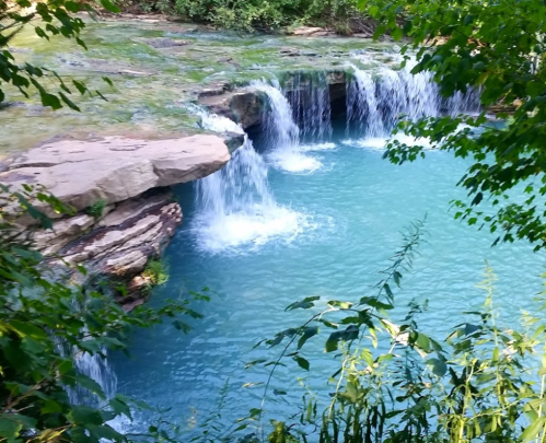 A serene waterfall cascading into a turquoise pool, surrounded by lush greenery and rocky terrain.