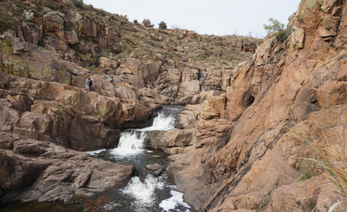 A rocky landscape with a small waterfall flowing through boulders and a person standing on the edge of the rocks.