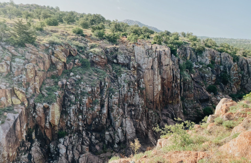 A rocky cliffside with greenery on top, overlooking a deep ravine in a natural landscape.