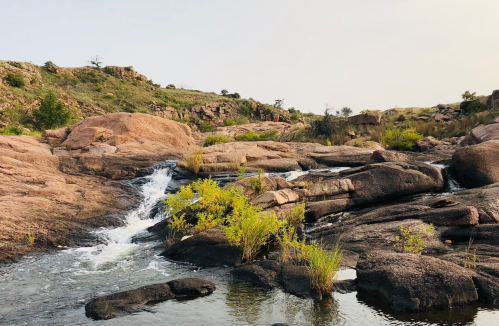 A serene landscape featuring a flowing river over rocky terrain, surrounded by greenery and gentle hills.