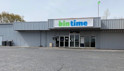 Exterior of a metal building with a large sign reading "bintime" and empty parking lot.