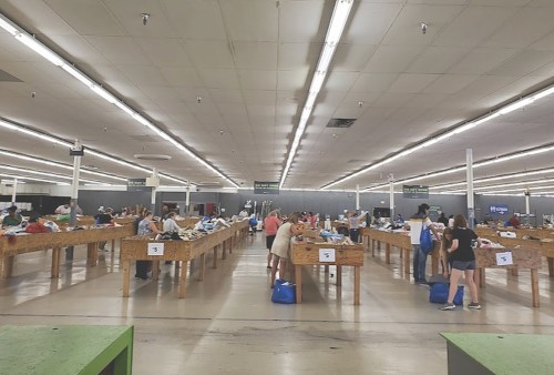 A spacious indoor market with long tables, people sorting through items, and bright overhead lights.