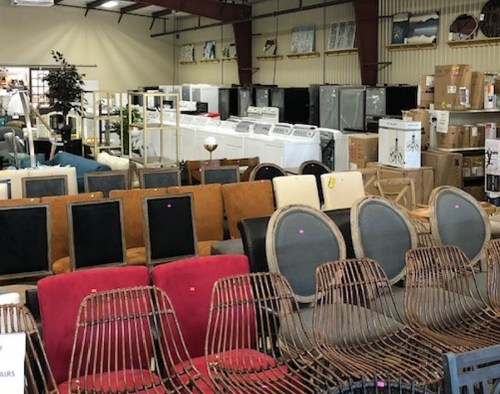 A variety of furniture and appliances displayed in a large warehouse setting.